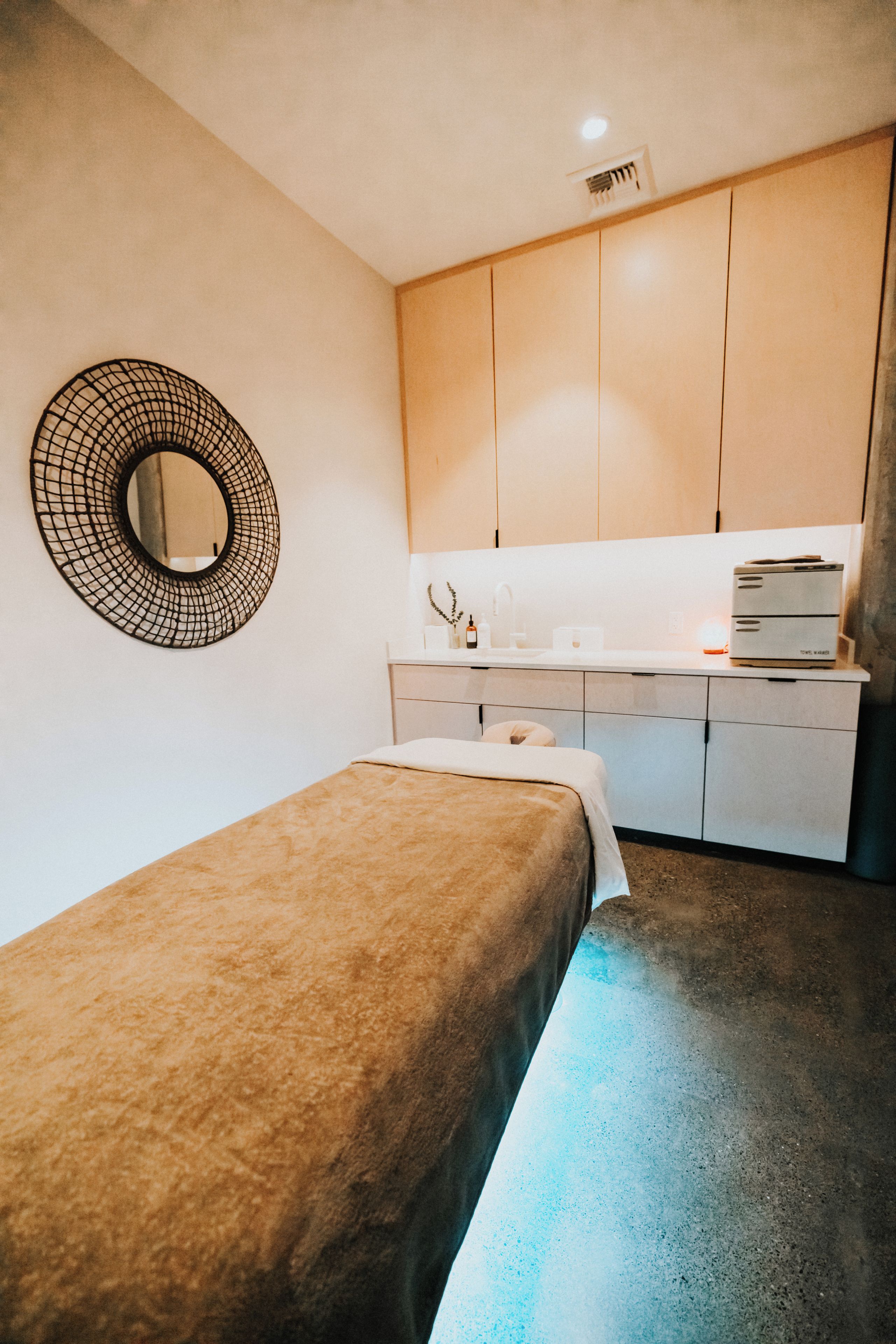 Un dormitori amb un llit individual, una petita taula de nit, un mirall i una zona d'espai kitchenette amb armaris i una superfície de treball.