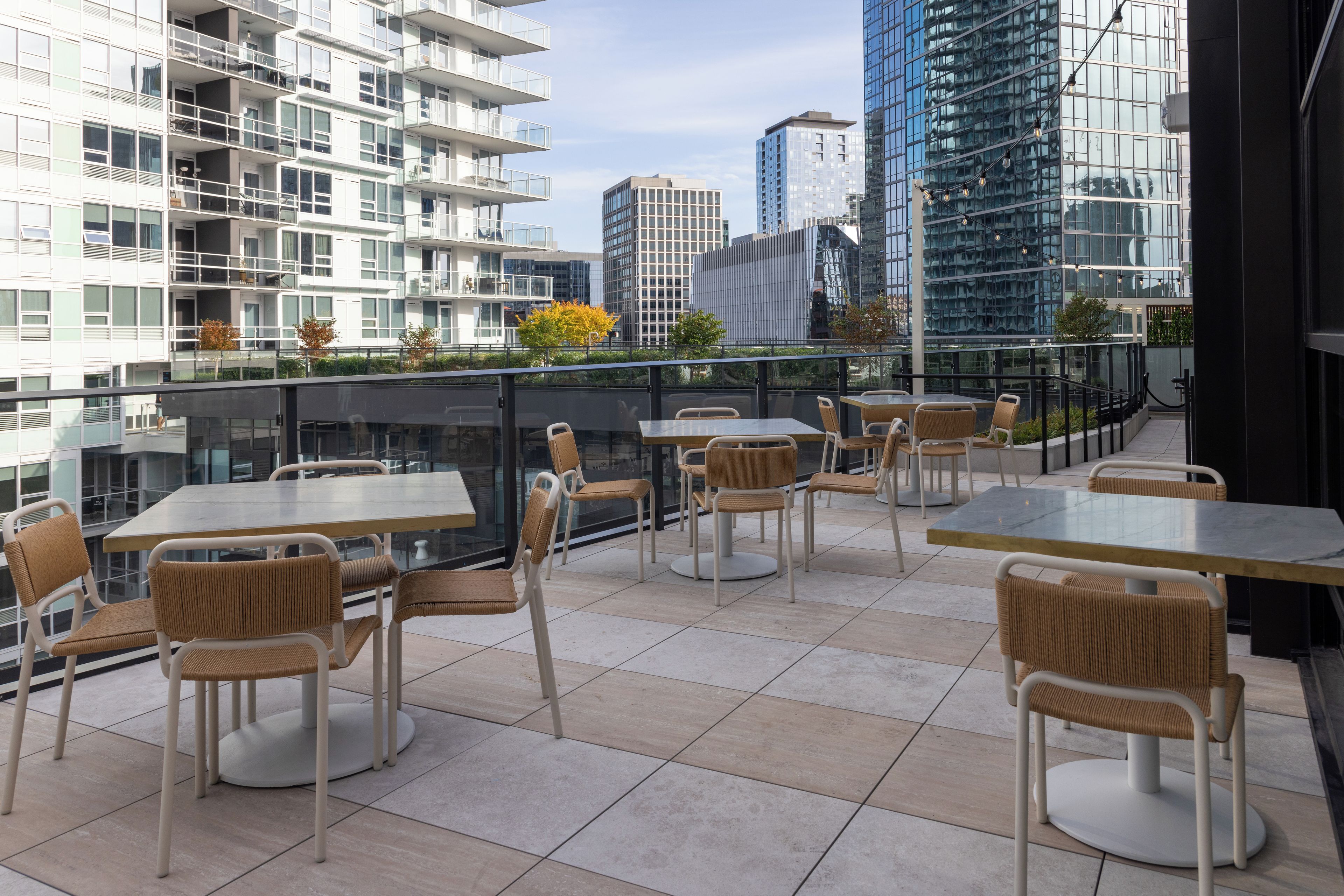 An outdoor terrace with tables and chairs, overlooking a cityscape with modern buildings.
