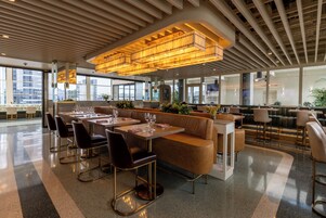 En moderne restaurant med høje lofter, store vinduer og forskellige siddepladser, herunder borde og båse.