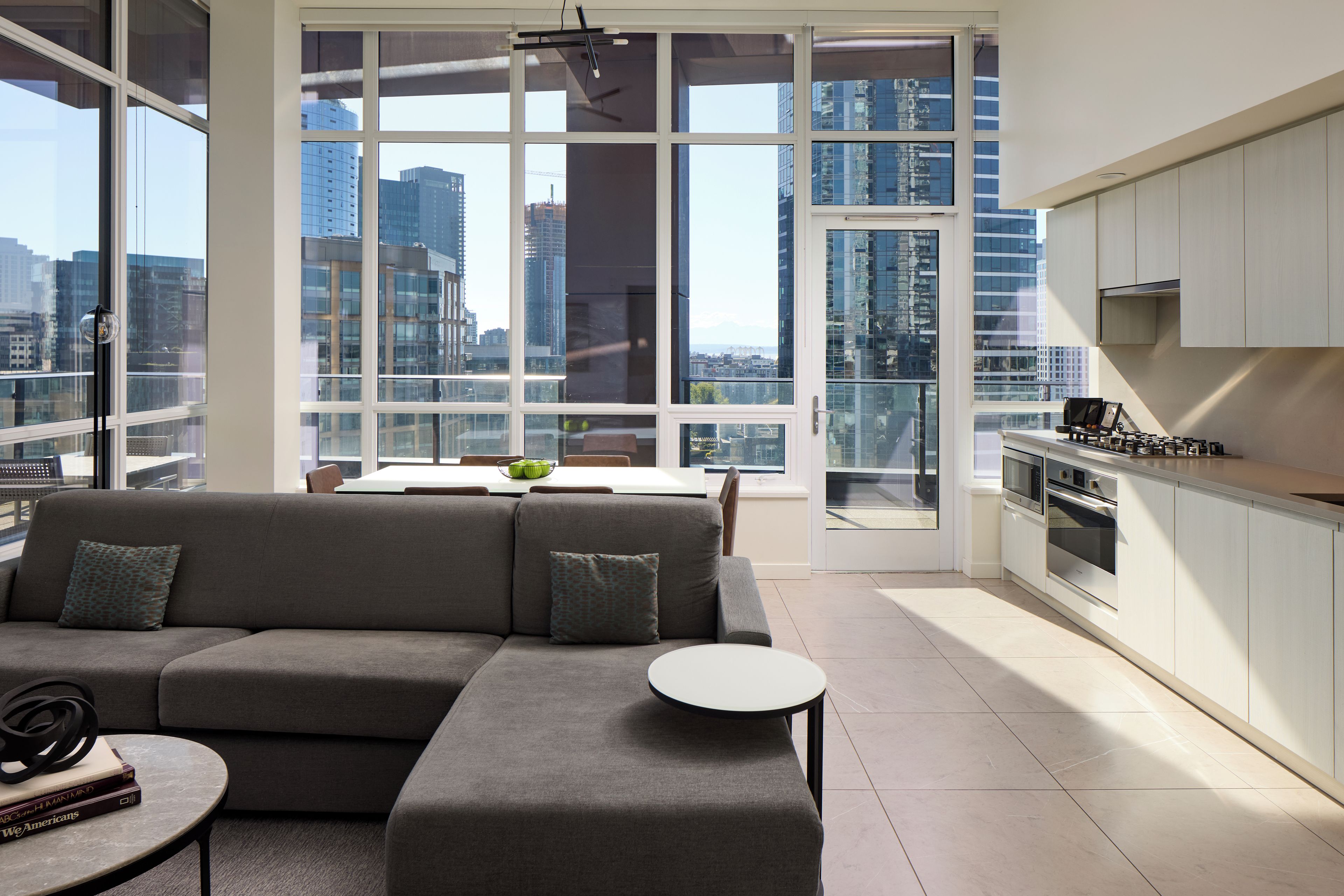 A modern living room with a sofa, a small round table, and a view of a cityscape through large windows.