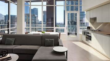 A modern living room with a sofa, a small round table, and a view of a cityscape through large windows.