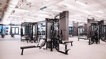 A gym with various exercise machines, benches, and a large window in the background.
