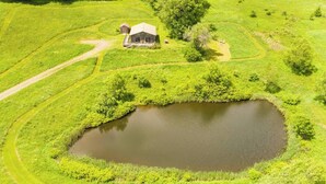 A rural landscape with a pond, a wooden house, and surrounding greenery. - Rustic 4 Season Cabin Getaway with Stunning Mountain Views (Hamden)