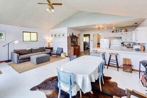 A spacious living area with a sofa, chairs, a dining table, and a kitchen in the background.