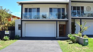 A two-story residential building with a garage, a balcony with chairs, and a small garden area. - Nimbus 14A McIntyre Street - Linen supplied (South West Rocks)