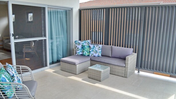 A balcony with a wicker sofa, two cushions, and a small table. - Nimbus 14A McIntyre Street - Linen supplied (South West Rocks)
