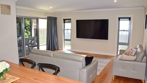 Relax in this stylish living room with a large flat-screen TV, comfortable sofa, and dining area leading to an outdoor space.