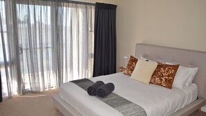 A hotel room with a large bed, a view through sheer curtains, and a nightstand with a lamp. - Nimbus 14A McIntyre Street - Linen supplied (South West Rocks)