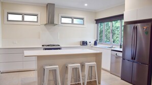 A modern kitchen with a large island, stainless steel appliances, and a view of greenery outside. - Nimbus 14A McIntyre Street - Linen supplied (South West Rocks)