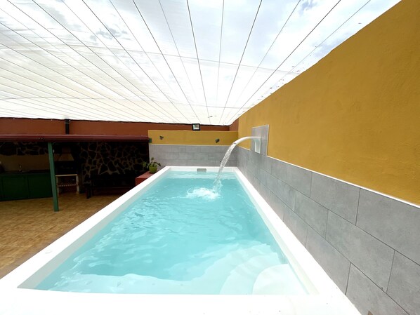 A rectangular swimming pool with a water feature, surrounded by a stone wall and a yellow wall. - Casa Benito Fagajesto (GALDAR)