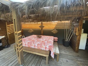 A wooden deck with a bed, a table, and a thatched roof. - Villa Brisson (Léognan)