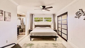Een slaapkamer met een bed, een plafondventilator, een raam met gordijnen, een deur met een ruit en een decoratie aan de muur.