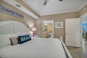 Un dormitorio con cama, mesita de noche, lámpara, puerta y un cartel que dice 'COASTAL LIVING'.