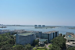 Un hotel moderno de gran altura con varias plantas, una piscina en la azotea y vista a un río y un puente al fondo.