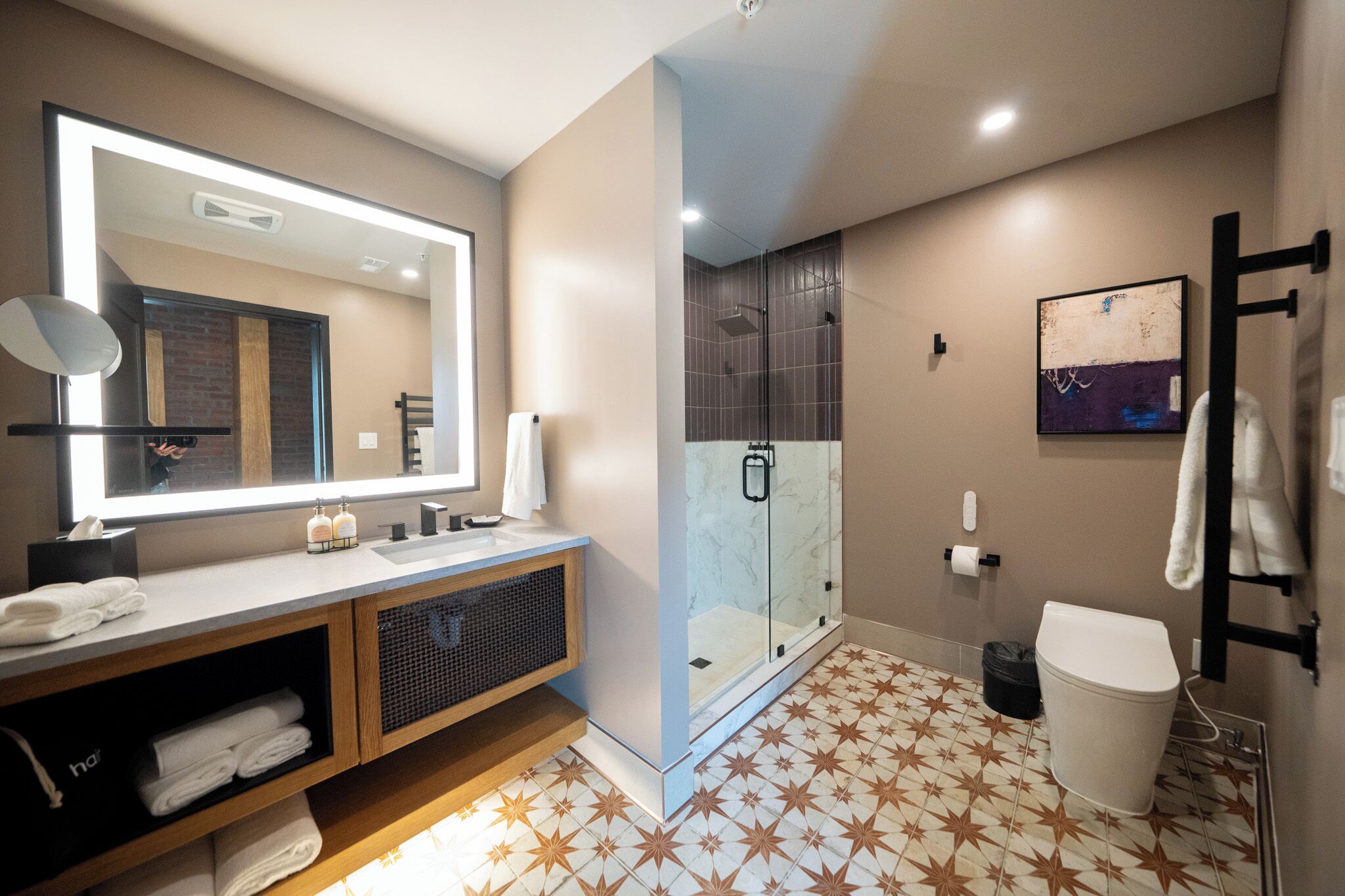 Une salle de bain moderne avec un grand miroir, une douche en verre, des toilettes blanches et un sol carrelé.