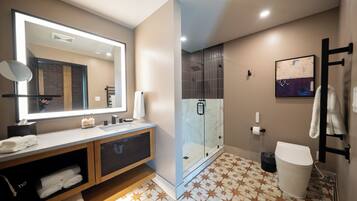 Une salle de bain moderne avec un grand miroir, une douche en verre, des toilettes blanches et un sol carrelé.
