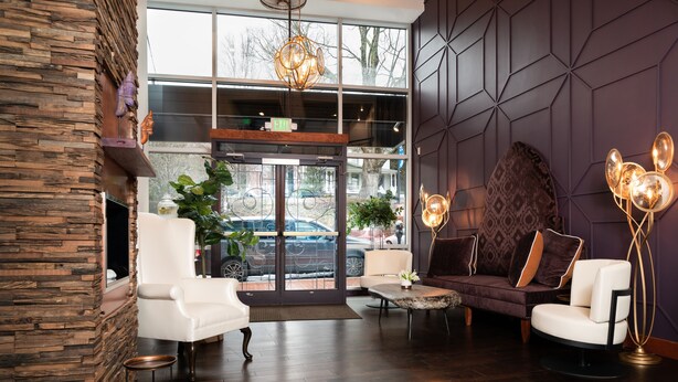 A modern lobby with a stone accent wall, a white armchair, a patterned sofa, and a large window with a view of the street. - The Horton Hotel and Rooftop Lounge (Boone)