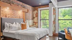 A bedroom with a brick wall, a large bed, and a view of greenery through the window. - The Horton Hotel and Rooftop Lounge (Boone)