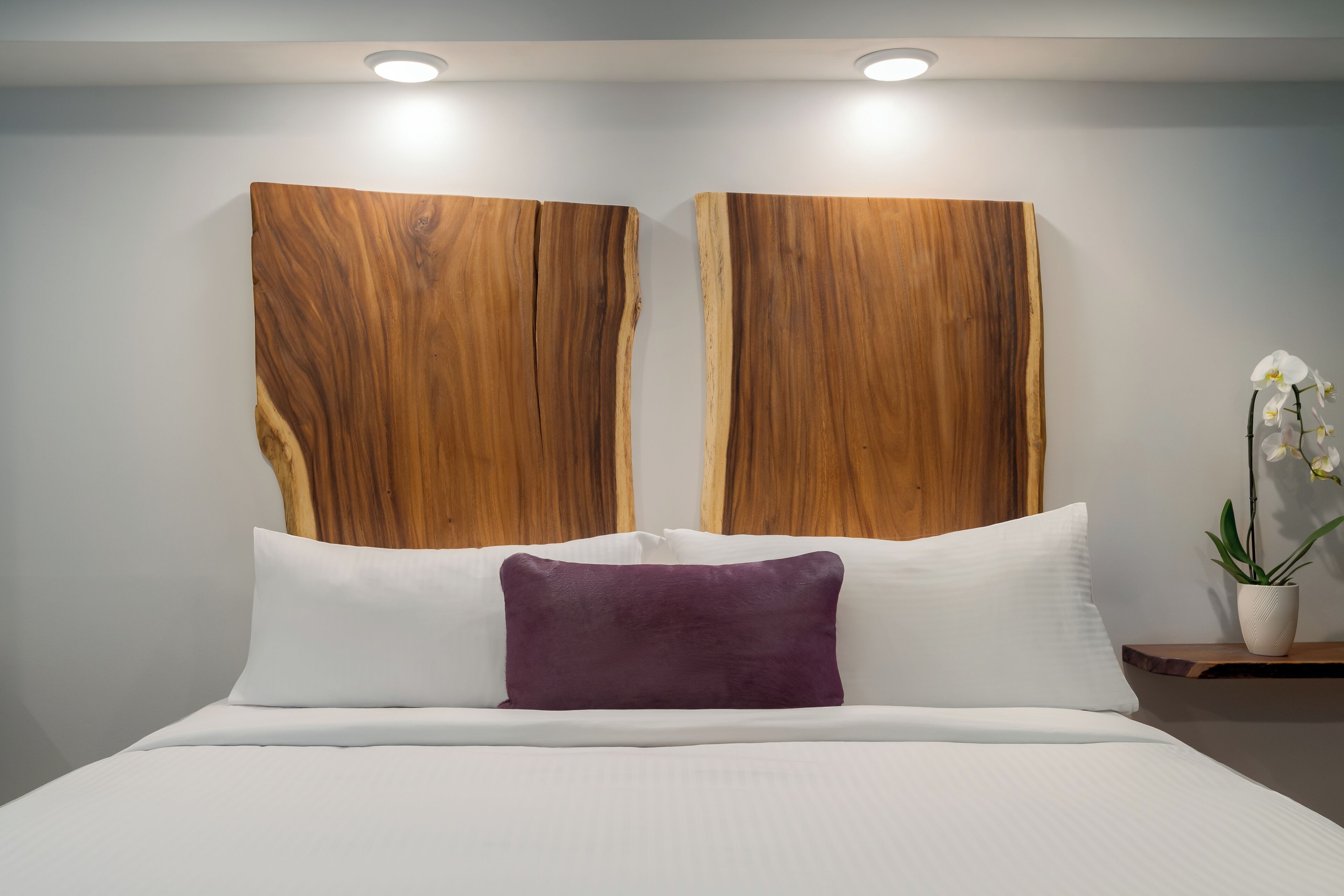 A bedroom with a bed, white pillows, a purple accent pillow, and a wooden headboard.
