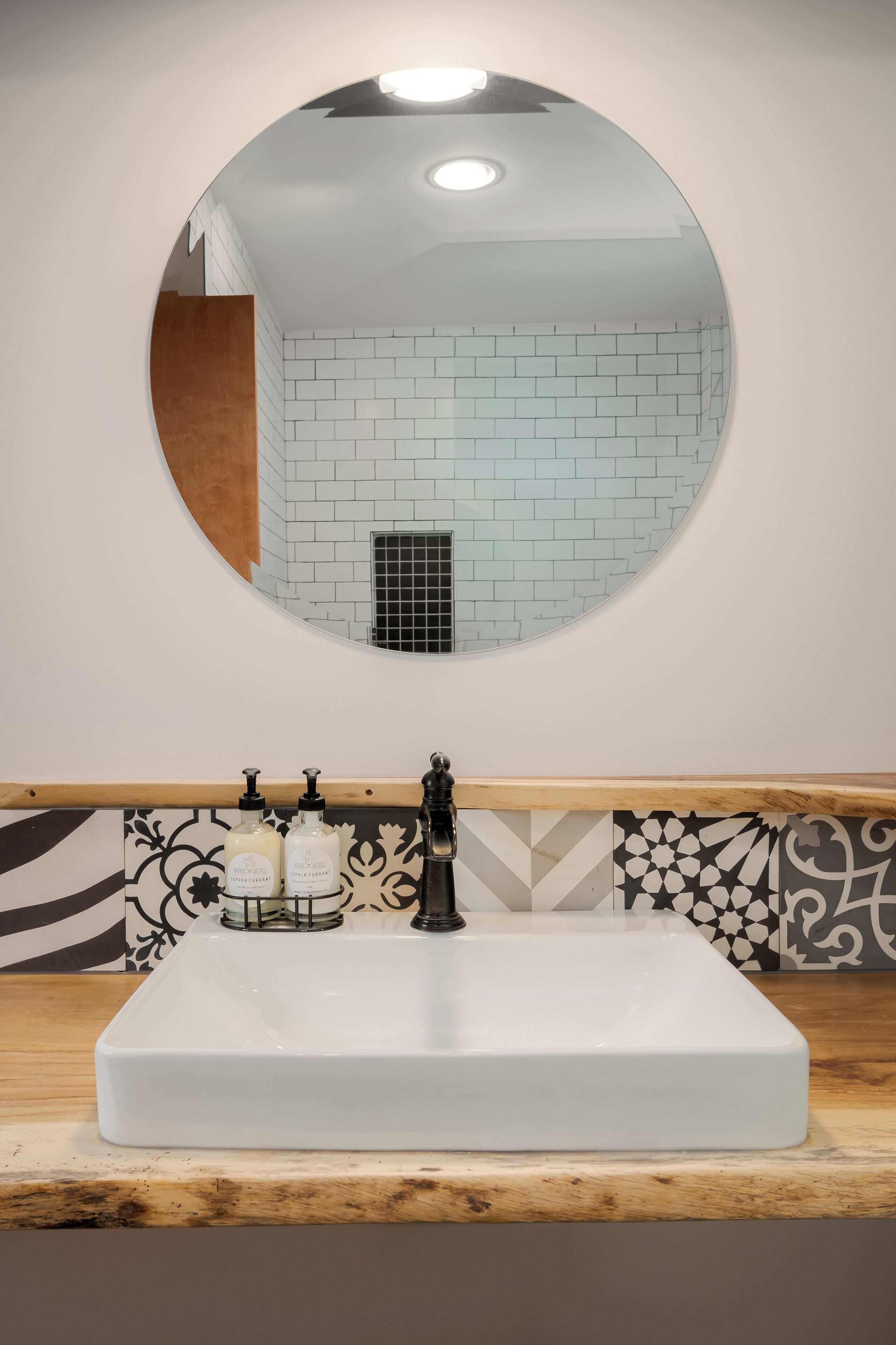 Een badkamer met een rechthoekig wastafelmeubel, een ronde spiegel en een betegelde wand.