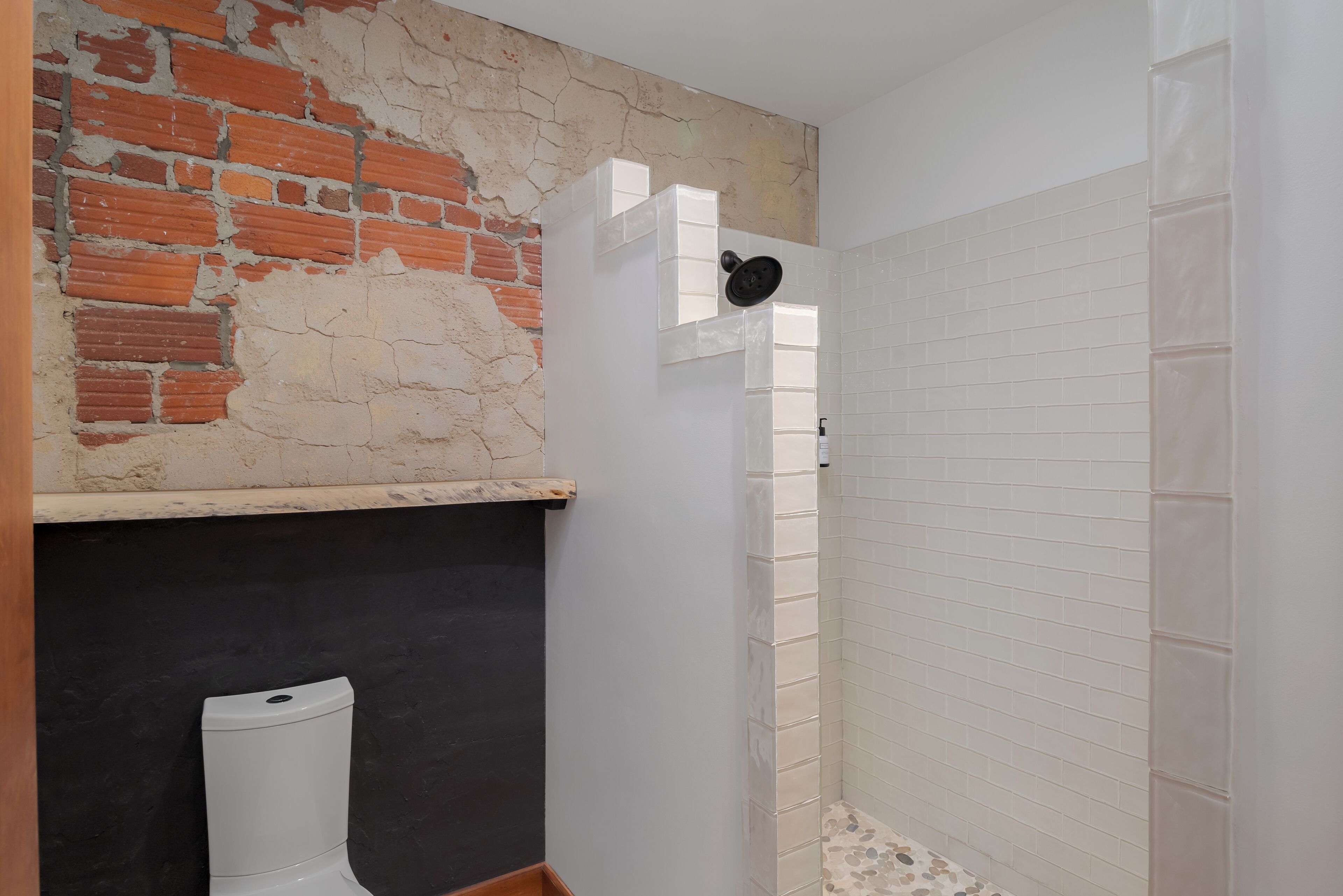 Ein Badezimmer mit Backsteinwand, weiß gefliester Dusche und Toilette.