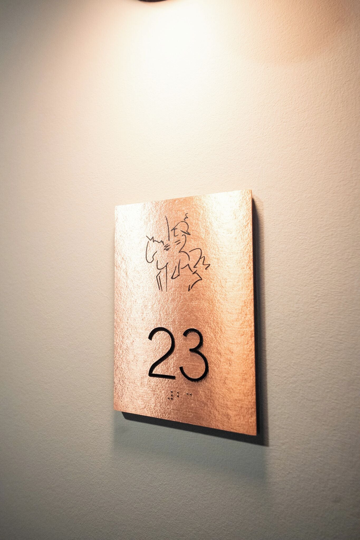 A wall-mounted sign with the number 23, featuring a textured surface and some handwritten text above the number.