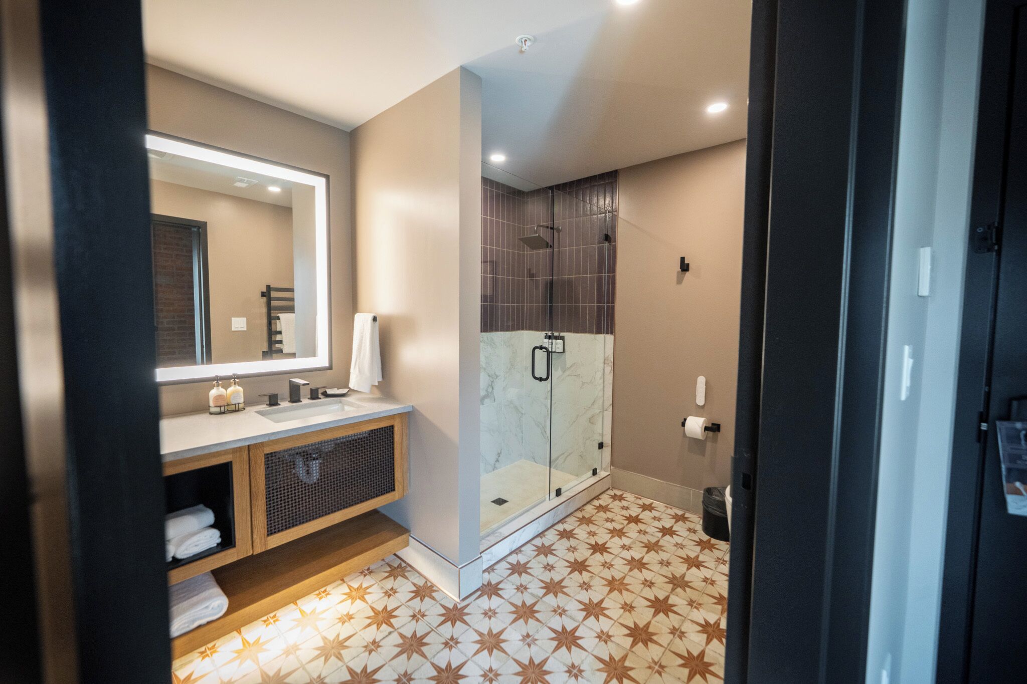 A modern bathroom with a large mirror, a shower with a glass door, and a tiled floor.