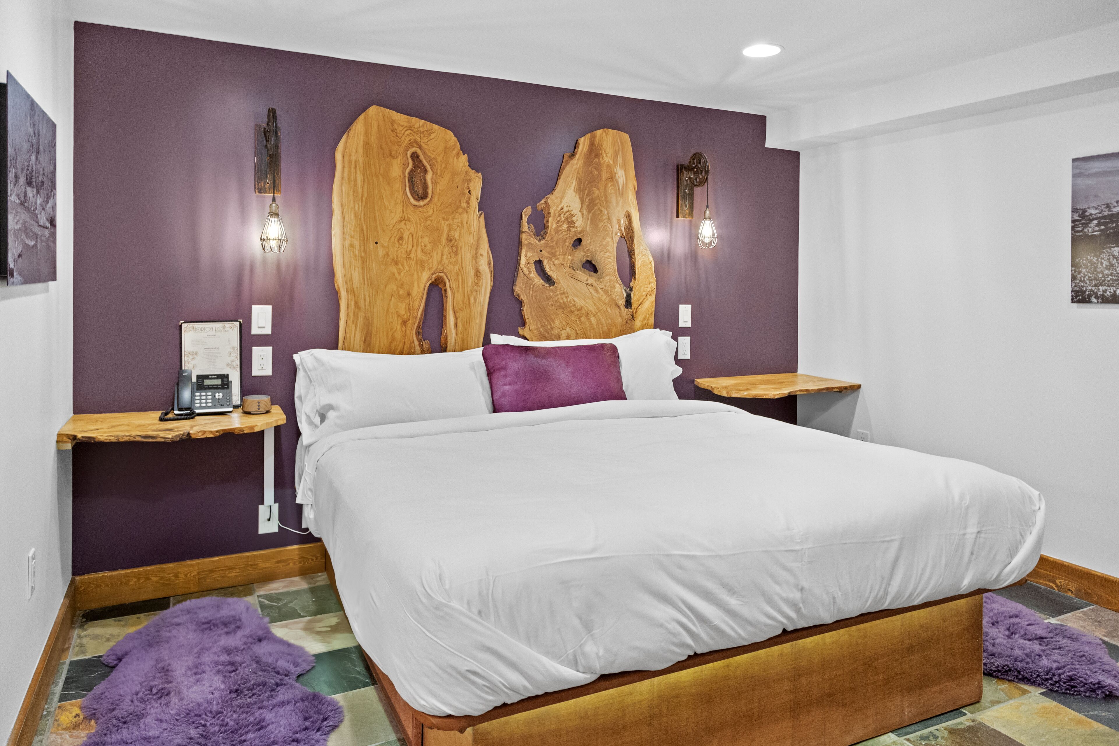 A bedroom with a large bed, purple walls, wooden headboard, and two nightstands with lamps.