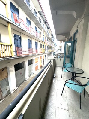 A balcony with a view of a building under construction. There are two chairs and a table on the balcony.