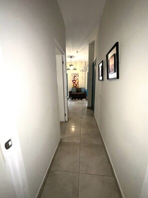 A narrow hallway with a tiled floor leading to a living area with a sofa and a coffee table.