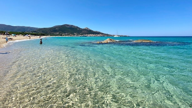 A beach with clear turquoise water, rocky outcrops, and a mountain in the background. - A Casa Piatatella (Aregno)
