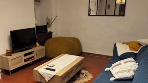 A living room with a sofa, a television on a wooden stand, a coffee table, and a chandelier. - A Casa Piatatella (Aregno)