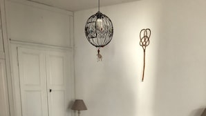 A bedroom with a large bed, a hanging light fixture, a wall decoration, and a bedside table with a lamp. - A Casa Piatatella (Aregno)
