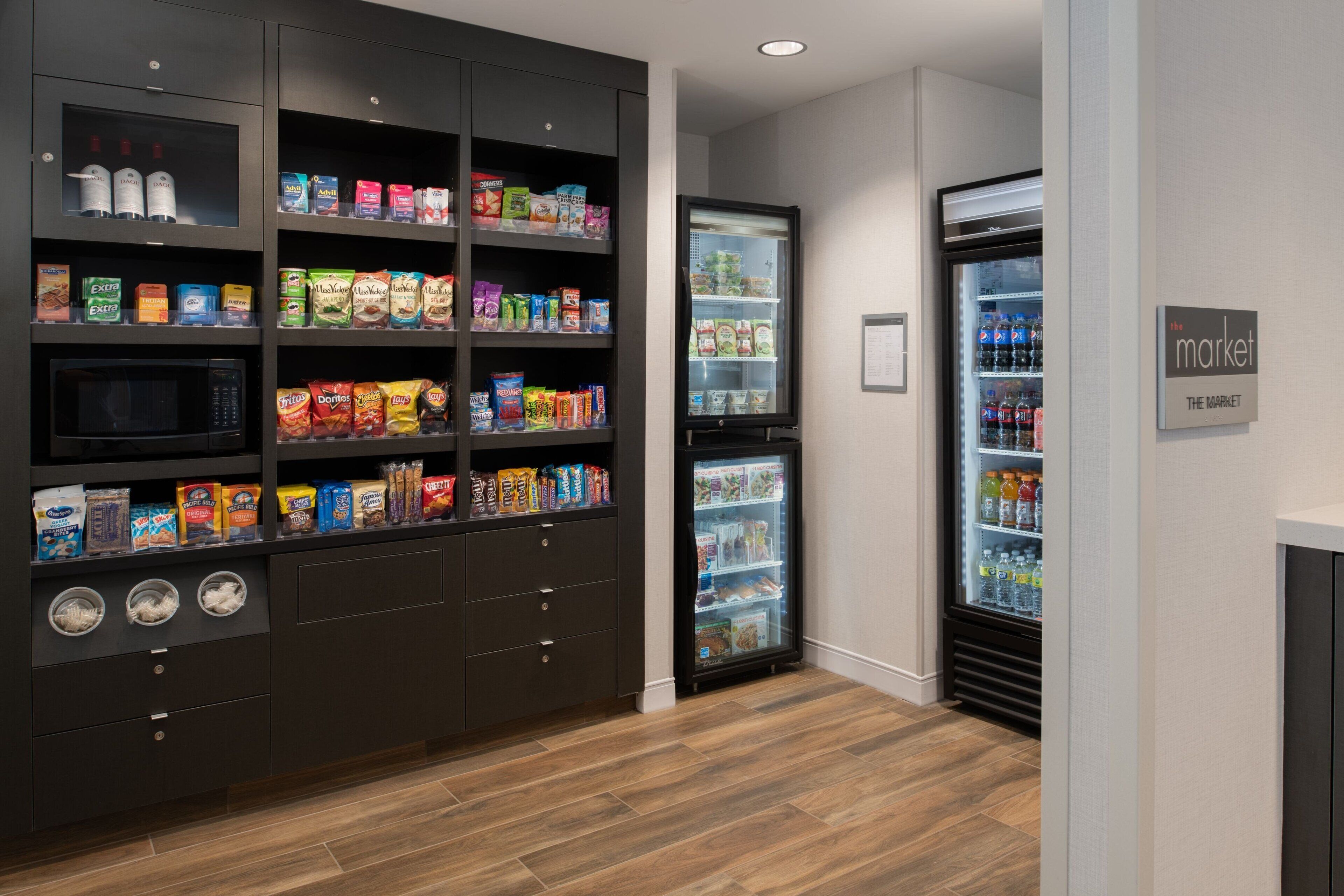 A kitchenette with a microwave, storage cabinets, and a refrigerator stocked with beverages and snacks.