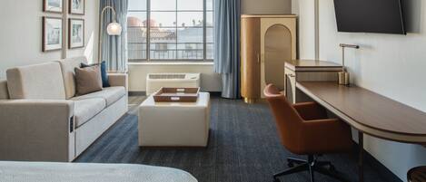 Hotelkamer met een bed, een bank, een bureau, een stoel, een televisie en een raam met gordijnen.