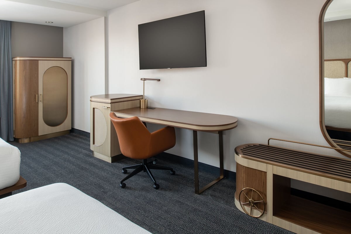A hotel room with a bed, a desk, a chair, a TV, a wardrobe, and a mirror.
