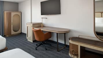 A hotel room with a bed, a desk, a chair, a TV, a wardrobe, and a mirror.