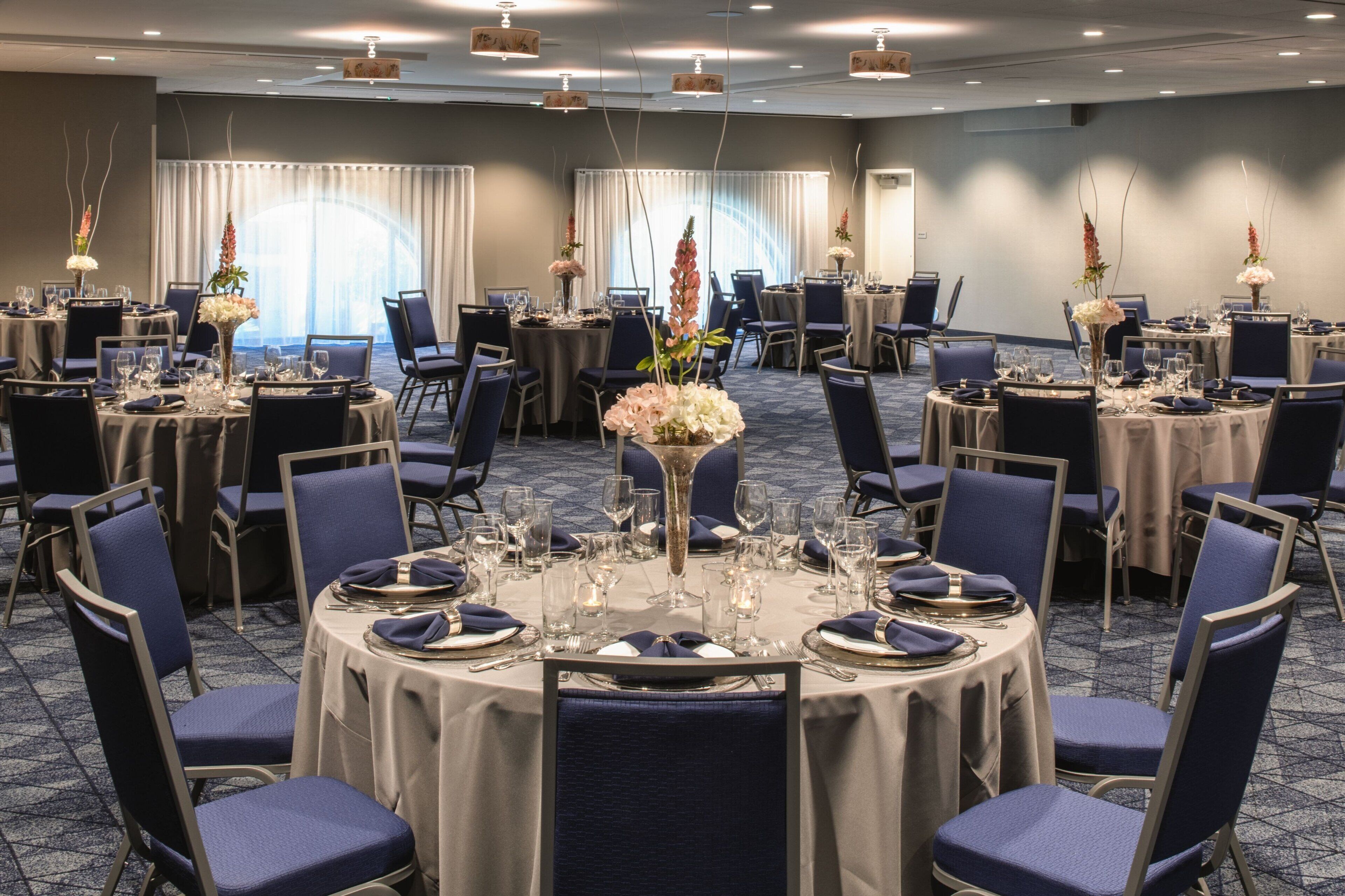 Une salle de conférence équipée de tables rondes, de chaises et agrémentée de compositions florales.
