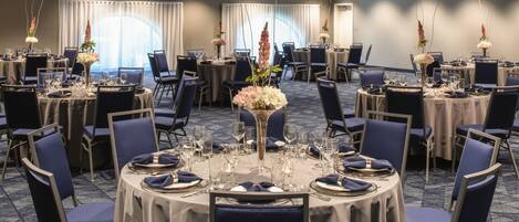 Une salle de conférence équipée de tables rondes, de chaises et agrémentée de compositions florales.