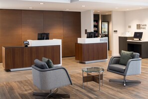 A reception area with two wooden reception desks, a glass coffee table, and two grey armchairs. - Courtyard by Marriott Santa Cruz (Santa Cruz)