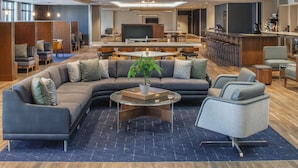A modern lounge area with a sectional sofa, a glass coffee table, and a bar with stools. - Courtyard by Marriott Santa Cruz (Santa Cruz)