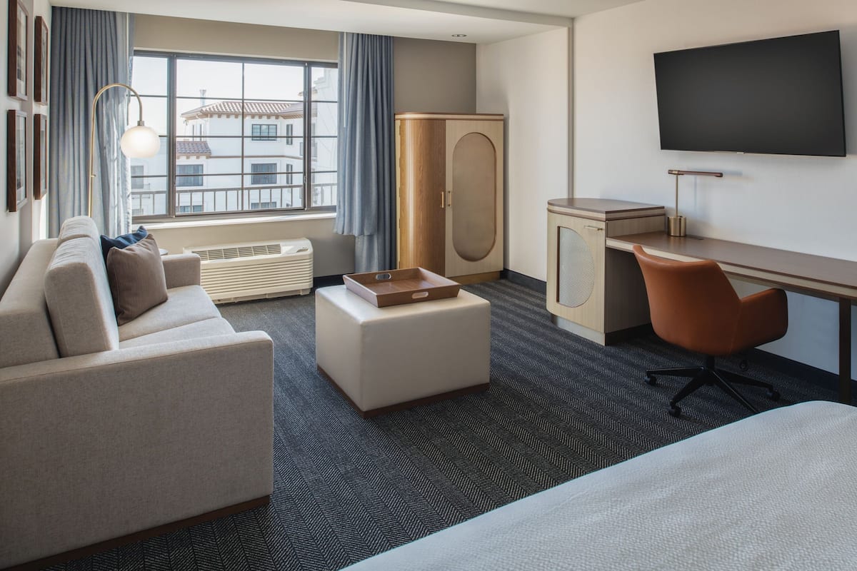 A hotel room with a sofa, a desk, a TV, a wardrobe, and a window with curtains.