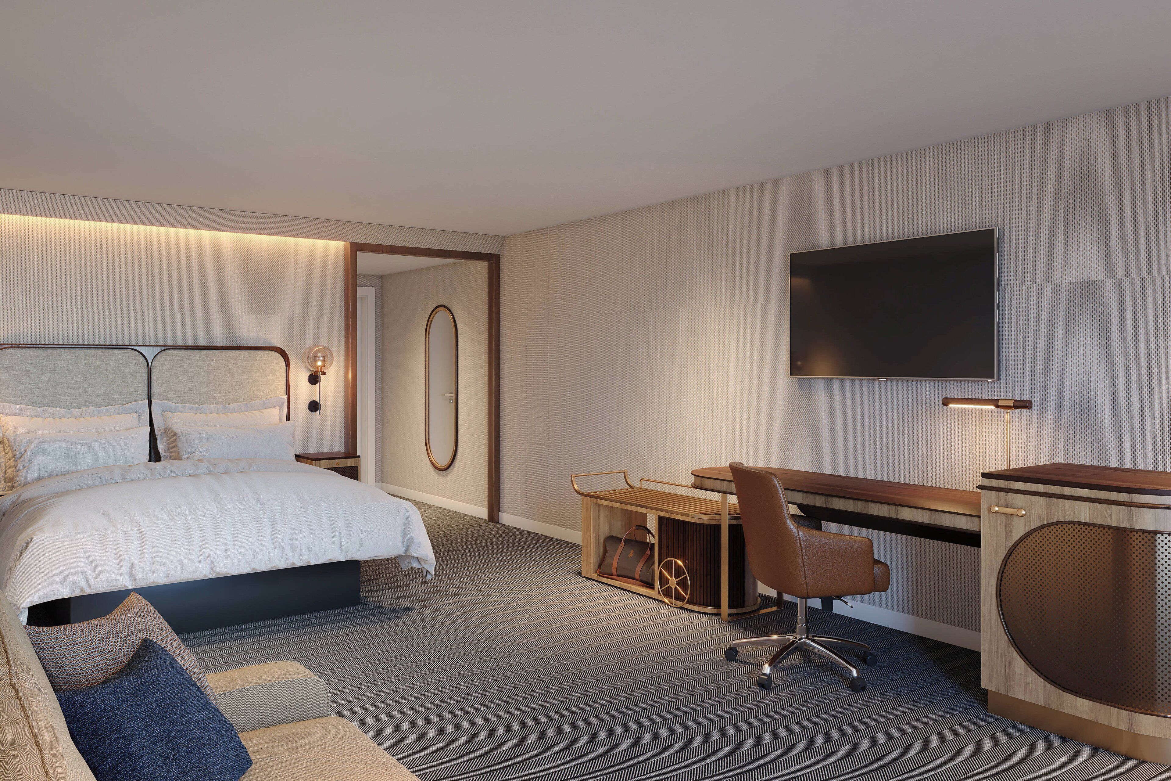 A modern hotel room with a large bed, a desk with a chair, a television, and a small seating area with cushions.