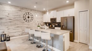 A modern kitchen with a large island, white cabinetry, stainless steel appliances, and a decorative clock on the wall. - 4808 LL Magical 4BR Disney Townhome Pool (Kissimmee)