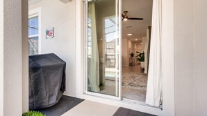 Ein überdachter Patio-Bereich mit Grill, eine Glasgleittür zu einem Innenraum mit Deckenventilator und einer Pflanze.