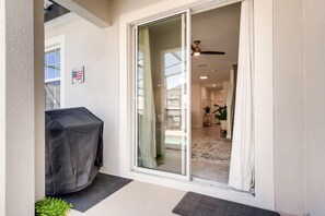 Eine überdachte Terrasse mit Grill, Glastüren zum Innenbereich mit Deckenventilator, Teppich und Pflanze.