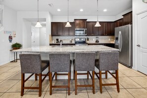Une cuisine dotée d’un grand îlot central, de meubles de rangement en bois foncé, d’appareils électroménagers en acier inoxydable et de quatre tabourets de bar.