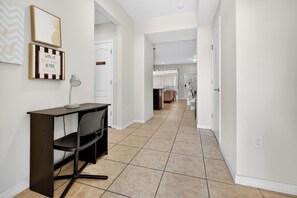 A hallway with a desk and chair, a door with a sign, and a tiled floor.