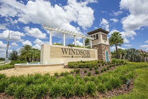 Placa indicando 'Windsor at Wildwood', com uma torre de pedra, pérgola e áreas verdes ajardinadas.