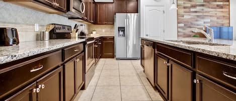 Una cocina moderna con armarios de madera oscura, electrodomésticos de acero inoxidable y piso de baldosas.
